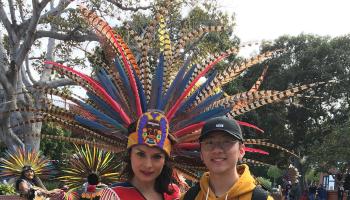 A woman with an elaborate costume with colorful feathers posing with a tour goer.